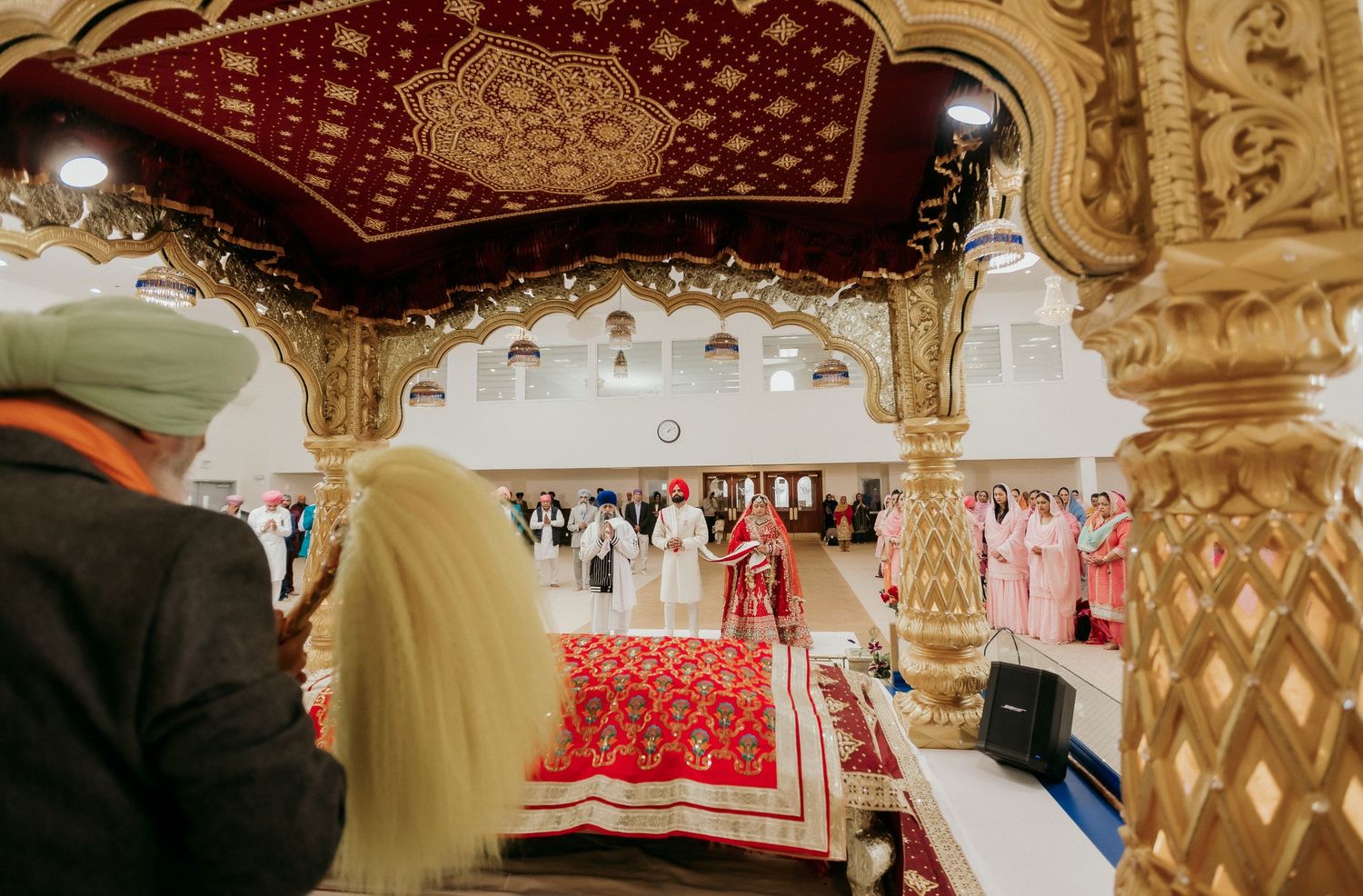 Traditional Sikh wedding ceremony viewed through ornate golden temple architecture.