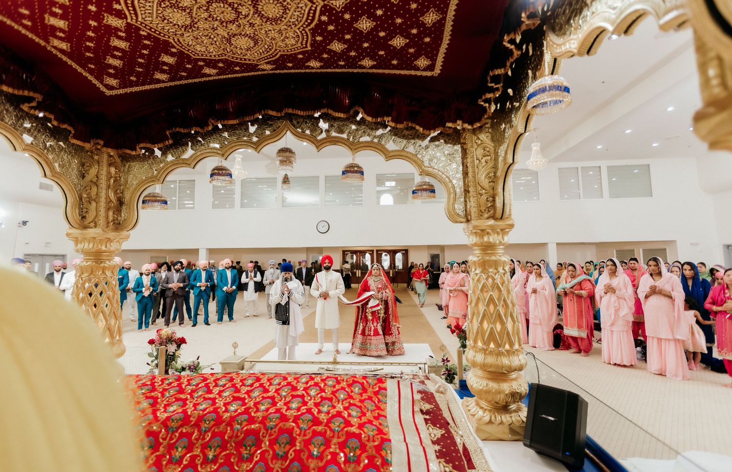 A wide view of a Sikh wedding ceremony through decorative temple archways with guests in attendance.