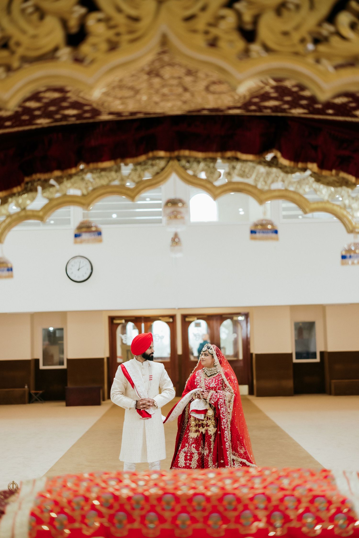 Traditional Sikh wedding ceremony taking place in an ornate temple hall with decorative arches.