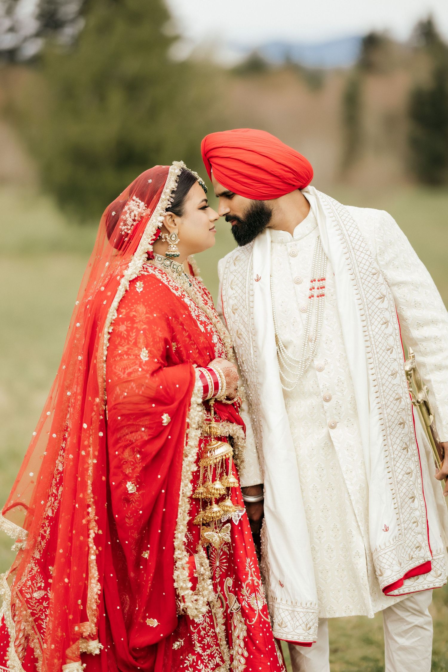 Romantic moment between couple in traditional Indian wedding attire against natural backdrop.