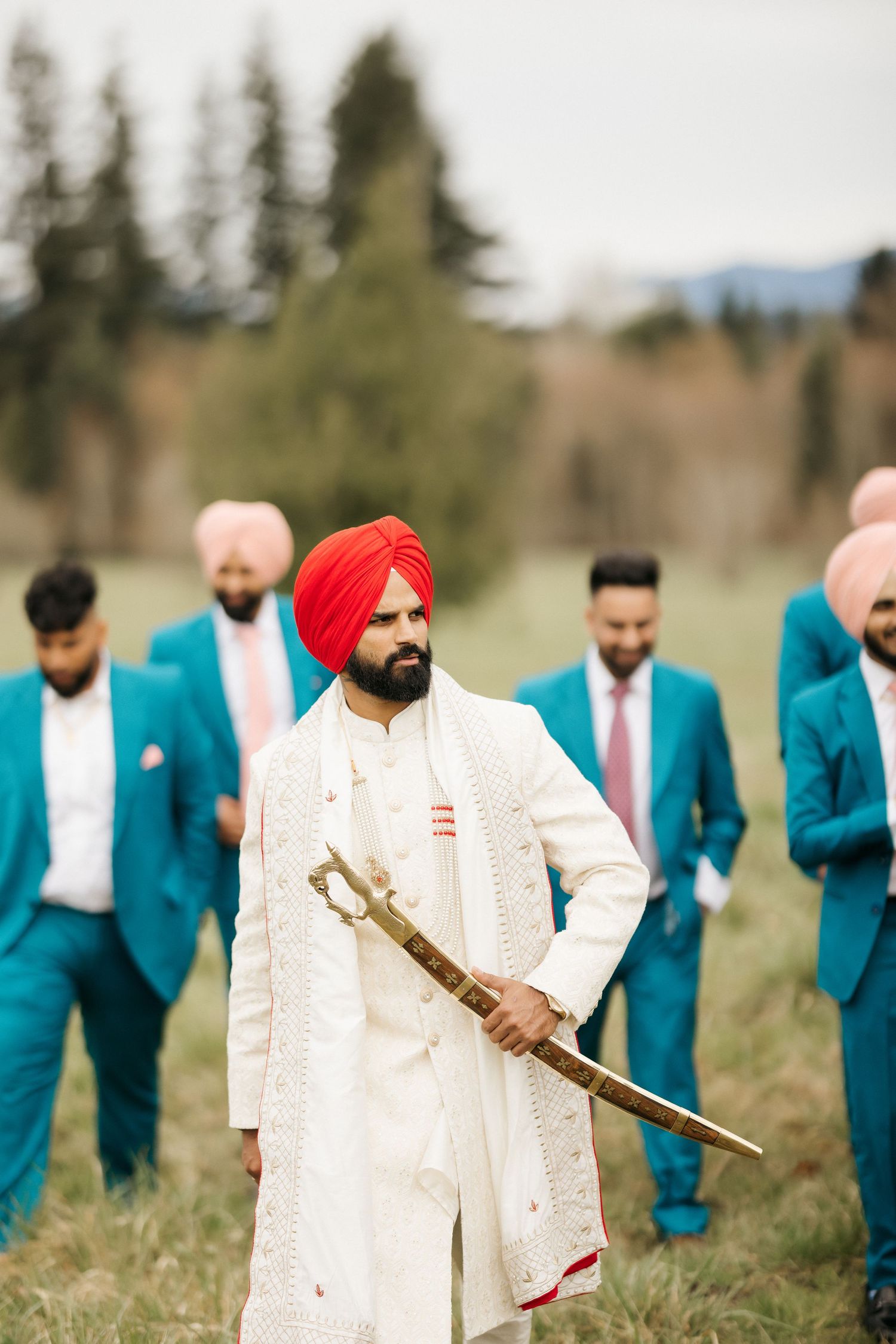 Groom in white traditional outfit with sword stands among groomsmen in turquoise suits.