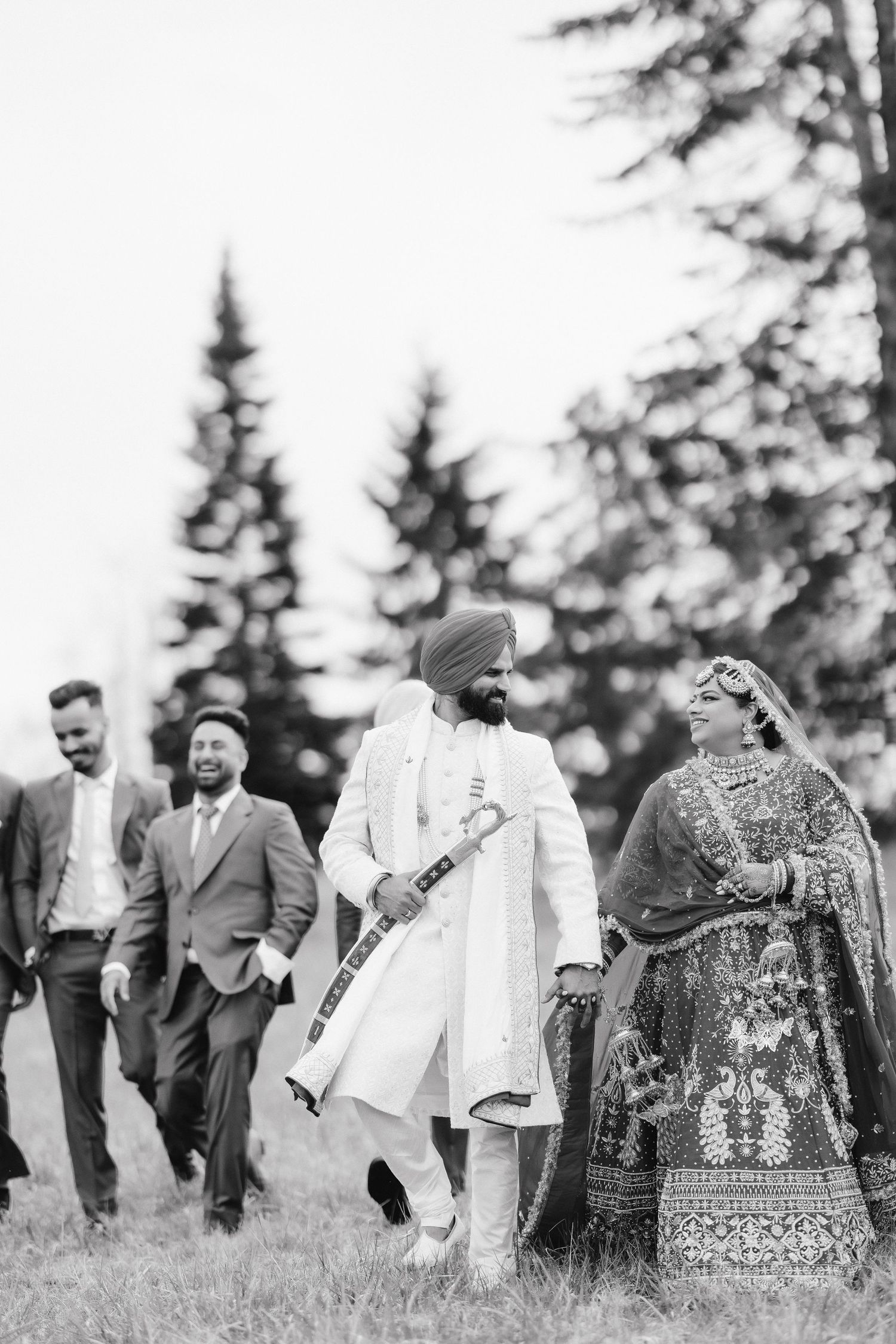 Black and white photo of a couple in traditional Indian wedding attire walking in a field.