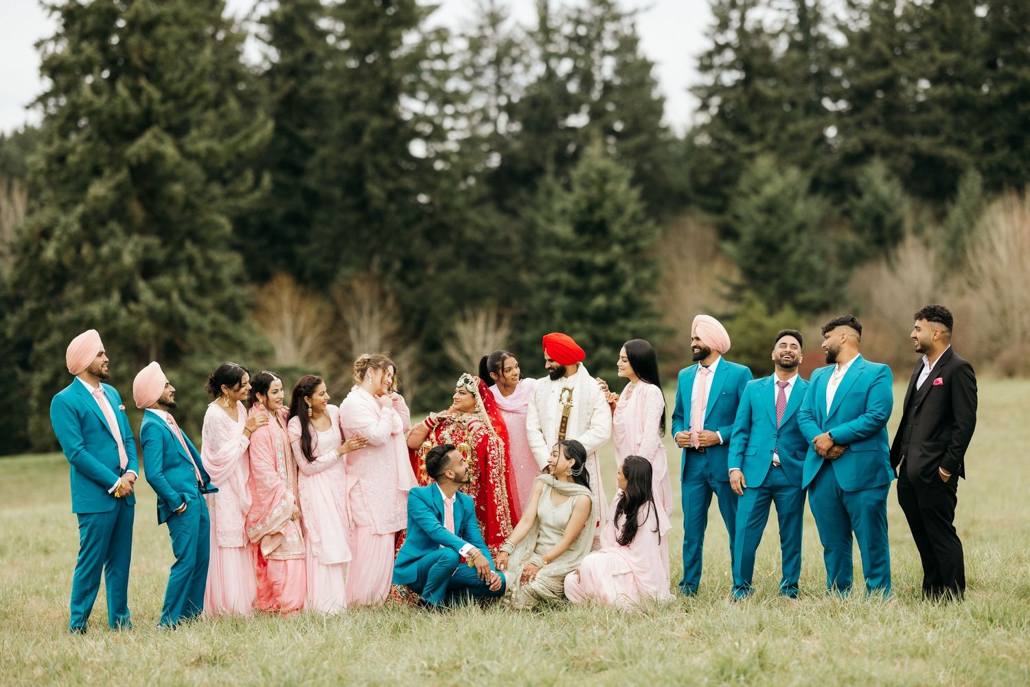 Wedding party gathered in a grassy field wearing coordinated pink and turquoise blue outfits.