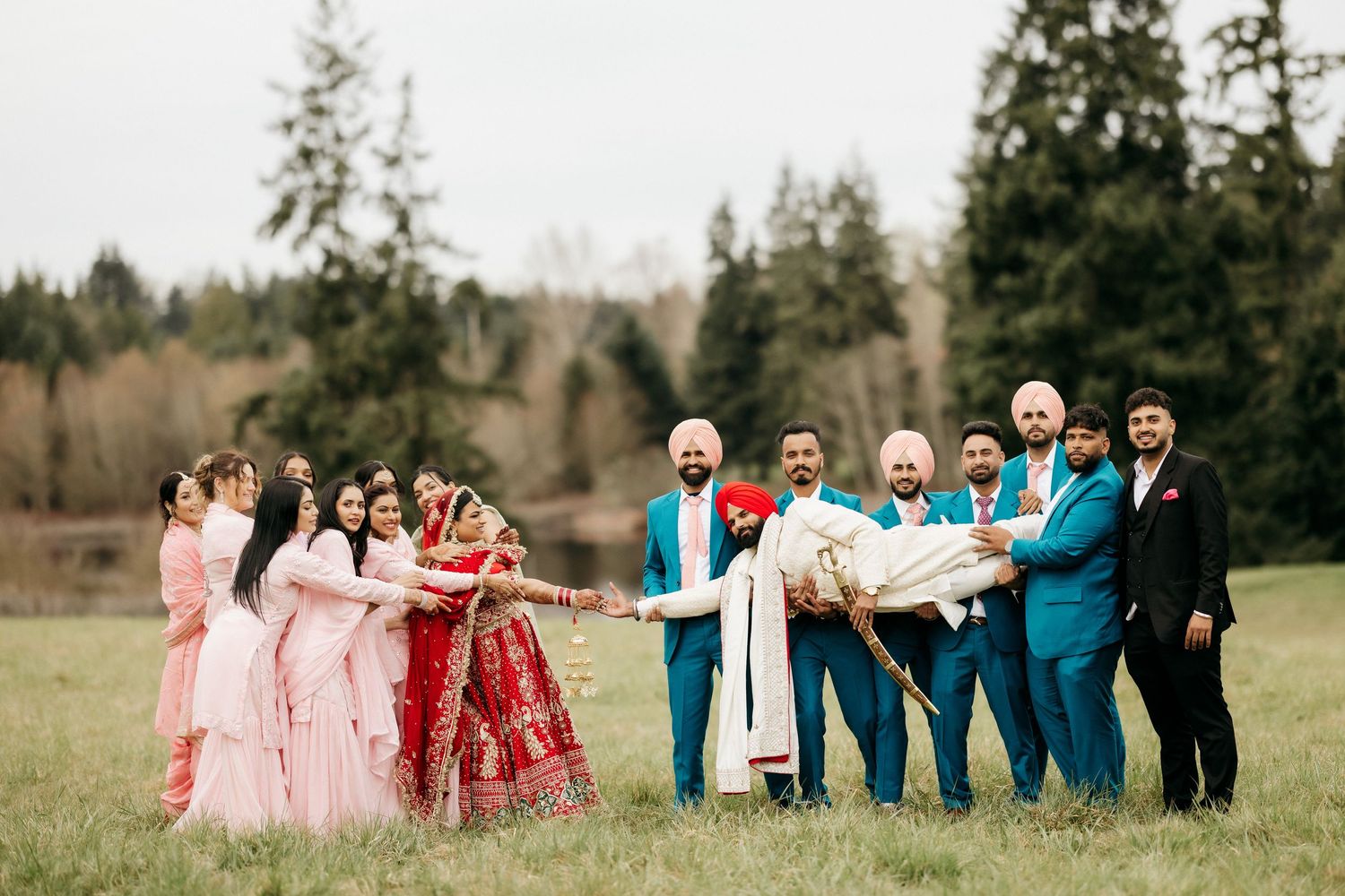 Wedding party poses playfully in a field with bridesmaids in pink and groomsmen in turquoise blue suits.