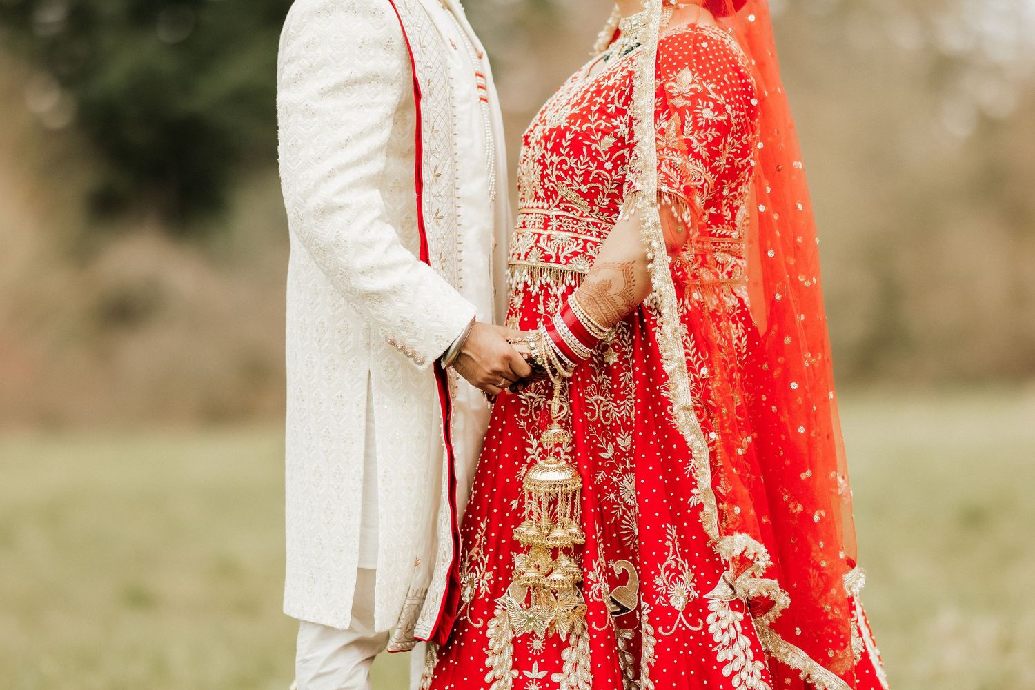 Detail shot of traditional Indian wedding couple's ornate red and ivory outfits.