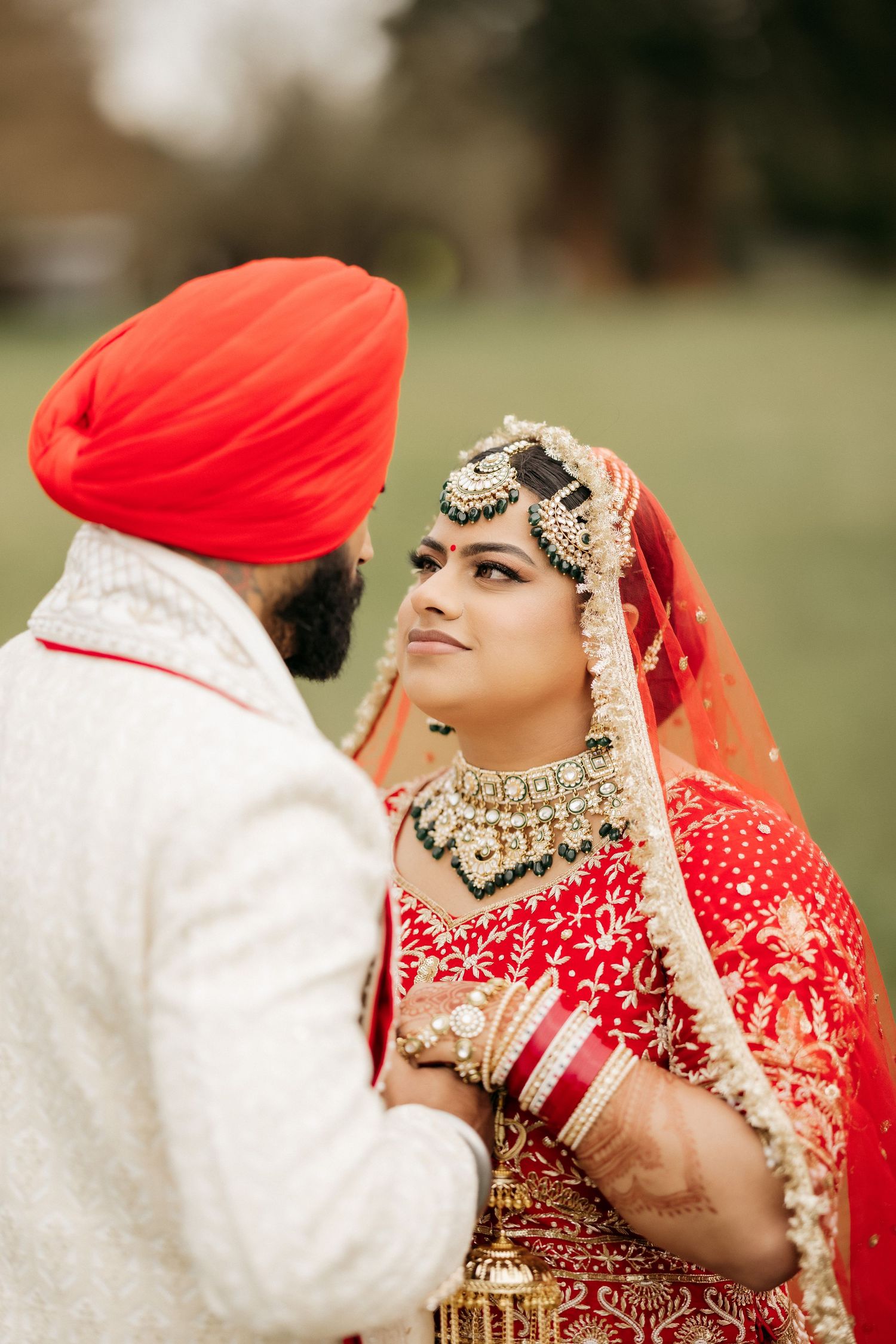 Close-up portrait of bride in traditional Indian wedding jewelry and attire with groom.