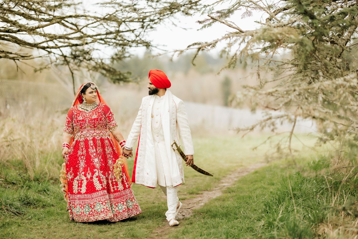 A couple in traditional wedding attire walks together on a path through nature.