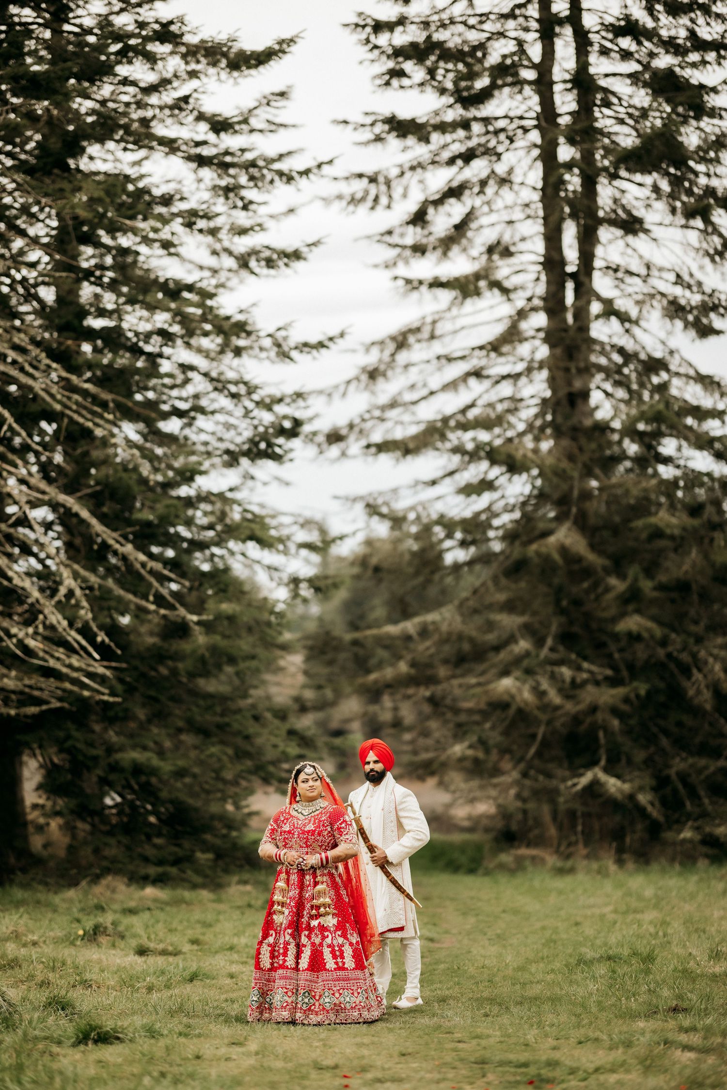 A couple in traditional wedding clothes photographed from afar in a misty forest setting.