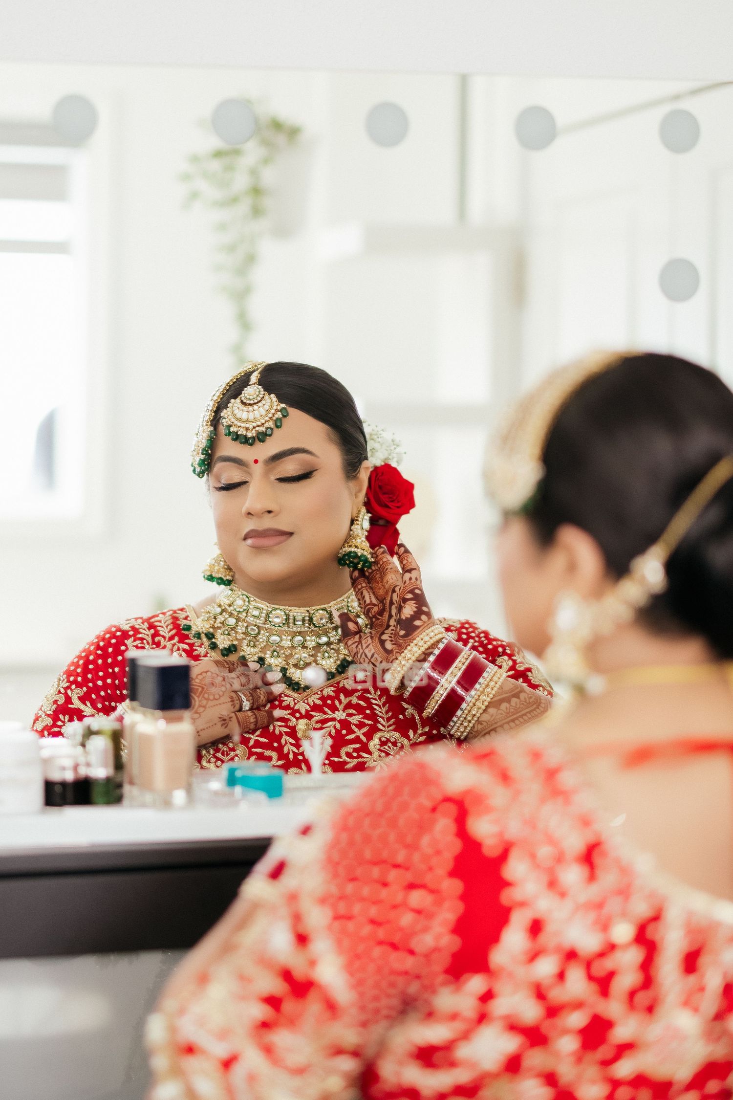 Mirror reflection of Indian bridal makeup and traditional red attire with gold jewelry.