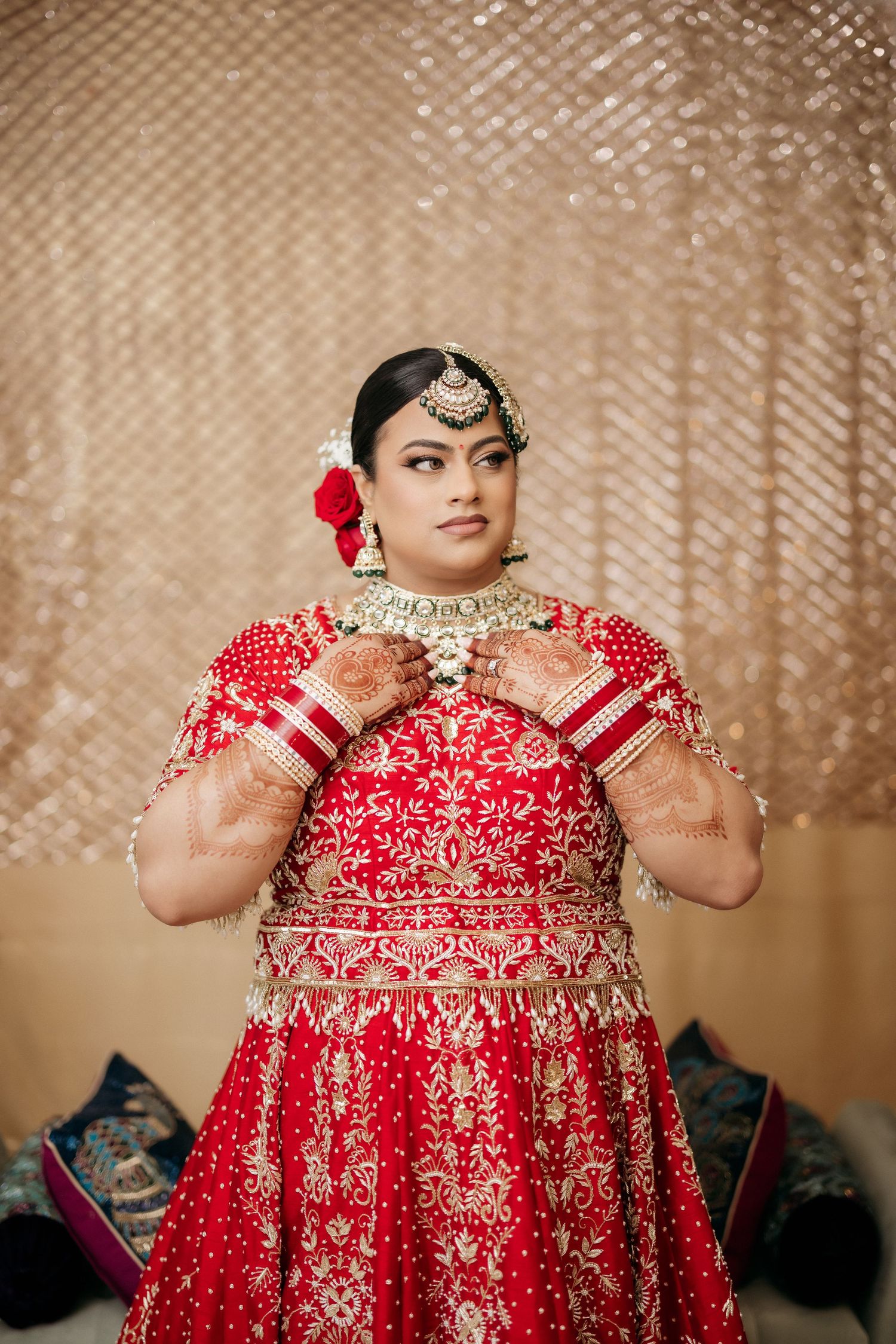 Traditional red and gold Indian bridal attire with ornate jewelry and henna decorated hands.