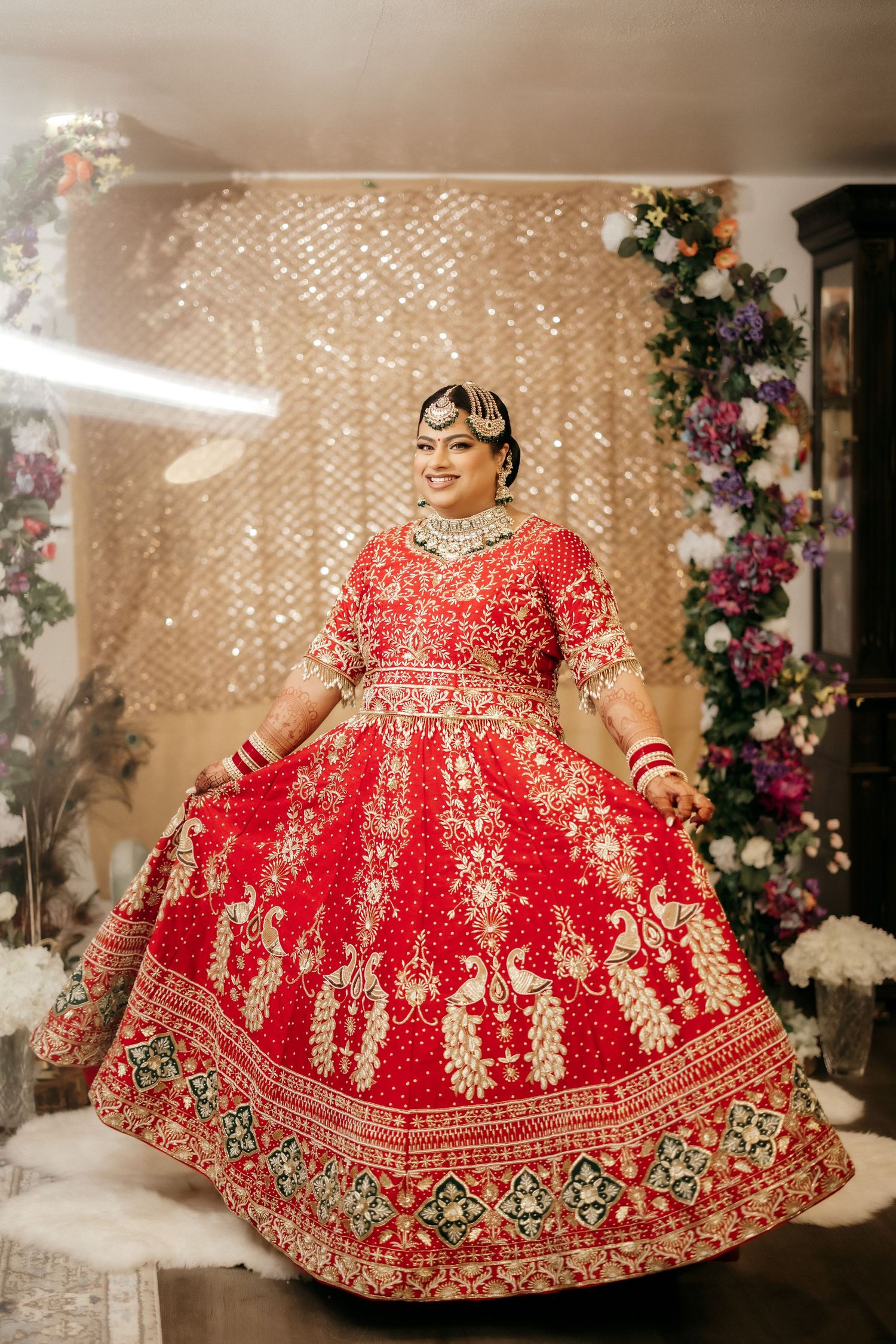 Traditional Indian bridal lehenga in red with gold embroidery against a sparkly backdrop with floral decorations.