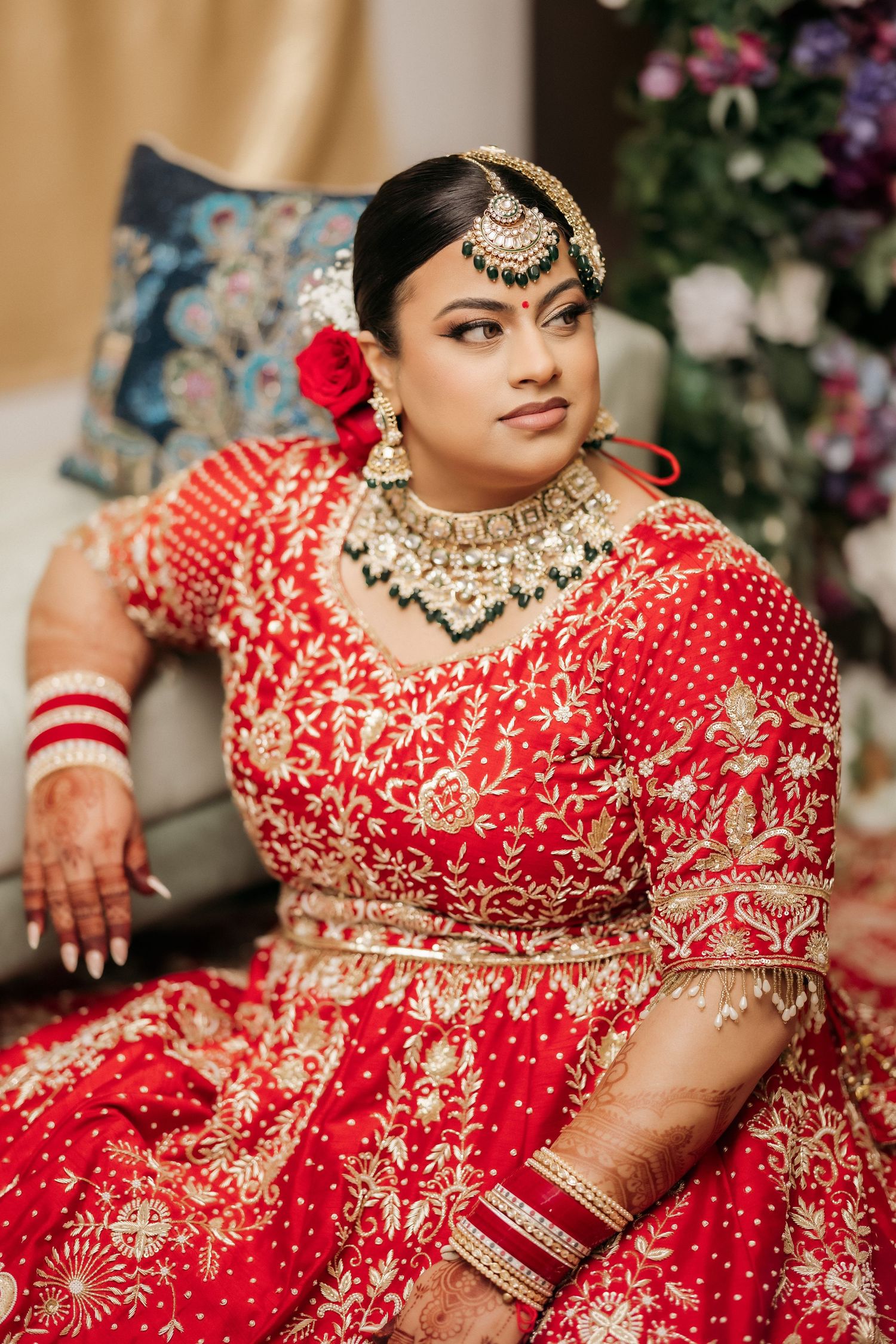 A bride in red embroidered lehenga with traditional Indian jewelry and makeup.
