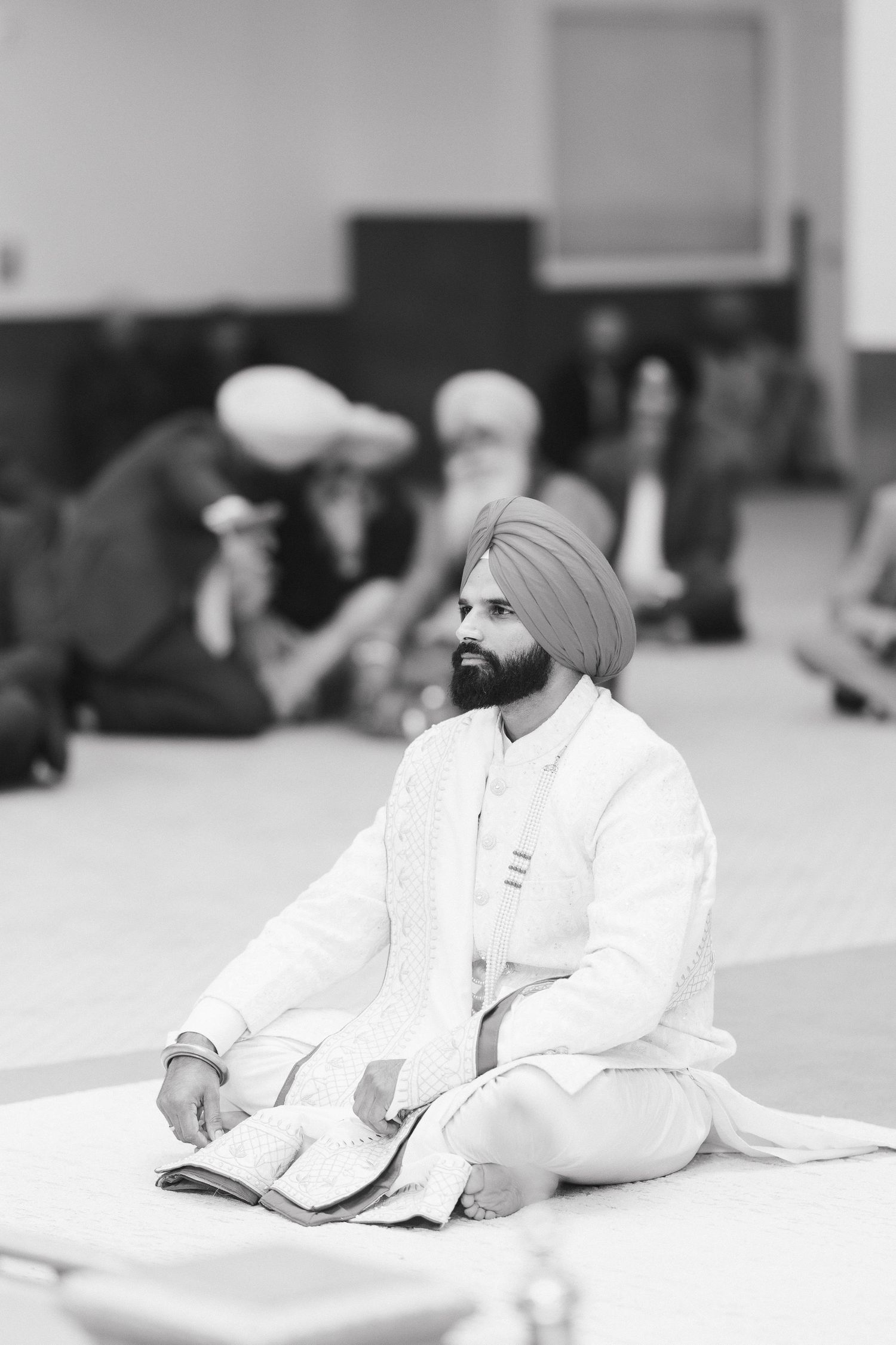 A person in white traditional dress sits in meditation pose during ceremony.