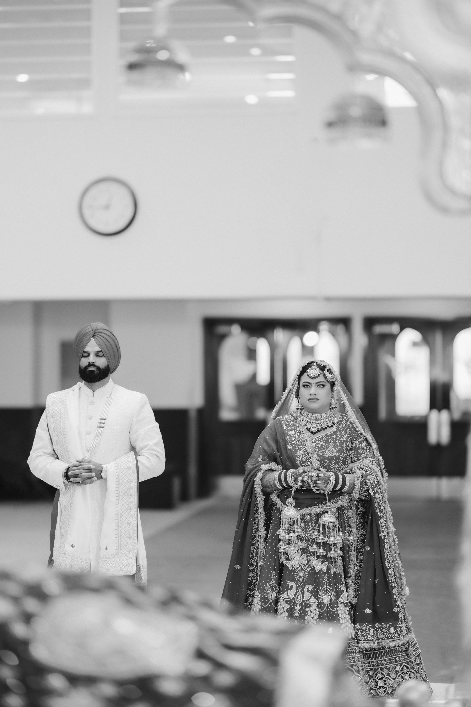 A couple stands in traditional Sikh wedding attire in black and white photography.