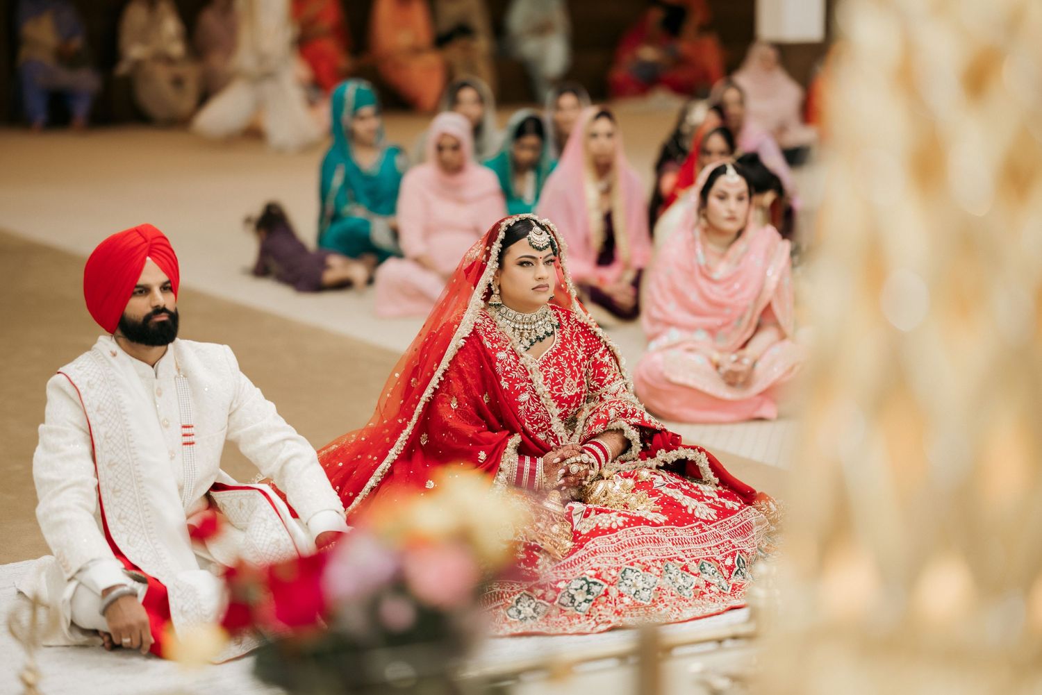 A traditional Sikh wedding ceremony with couple seated on floor in ornate decorations.