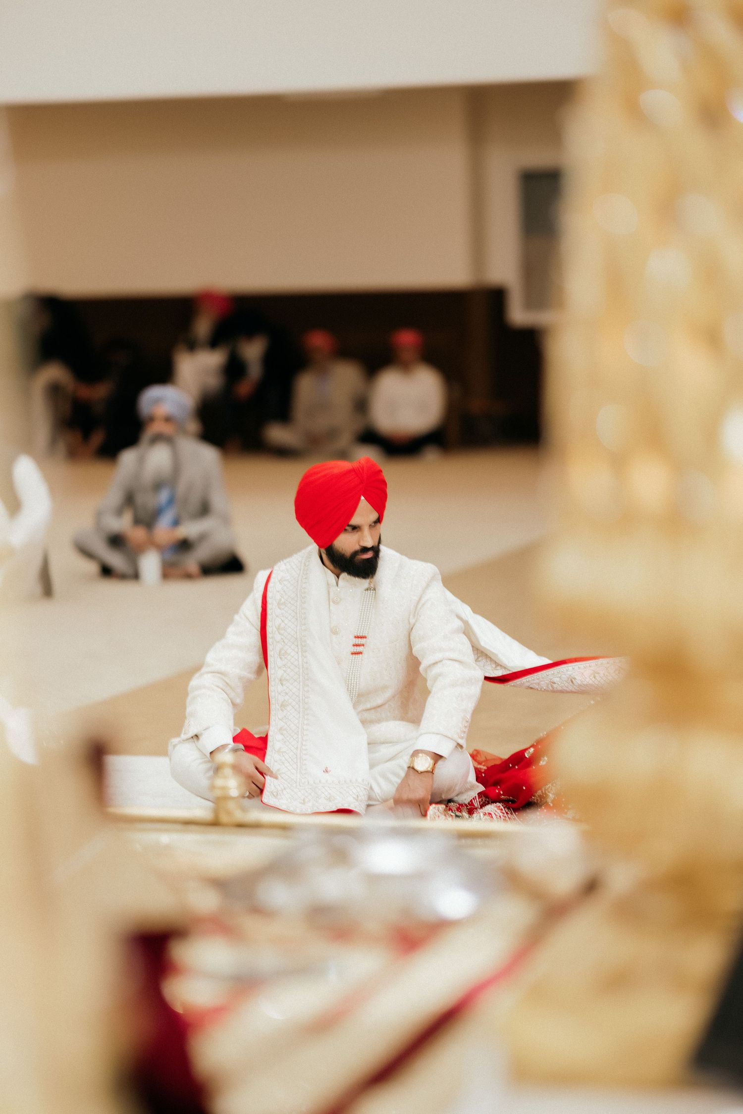 A person in a white kurta and red turban sits during a traditional Sikh ceremony.