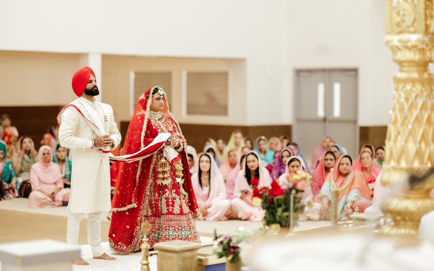 A Sikh wedding ceremony with the couple standing during traditional rituals surrounded by guests.