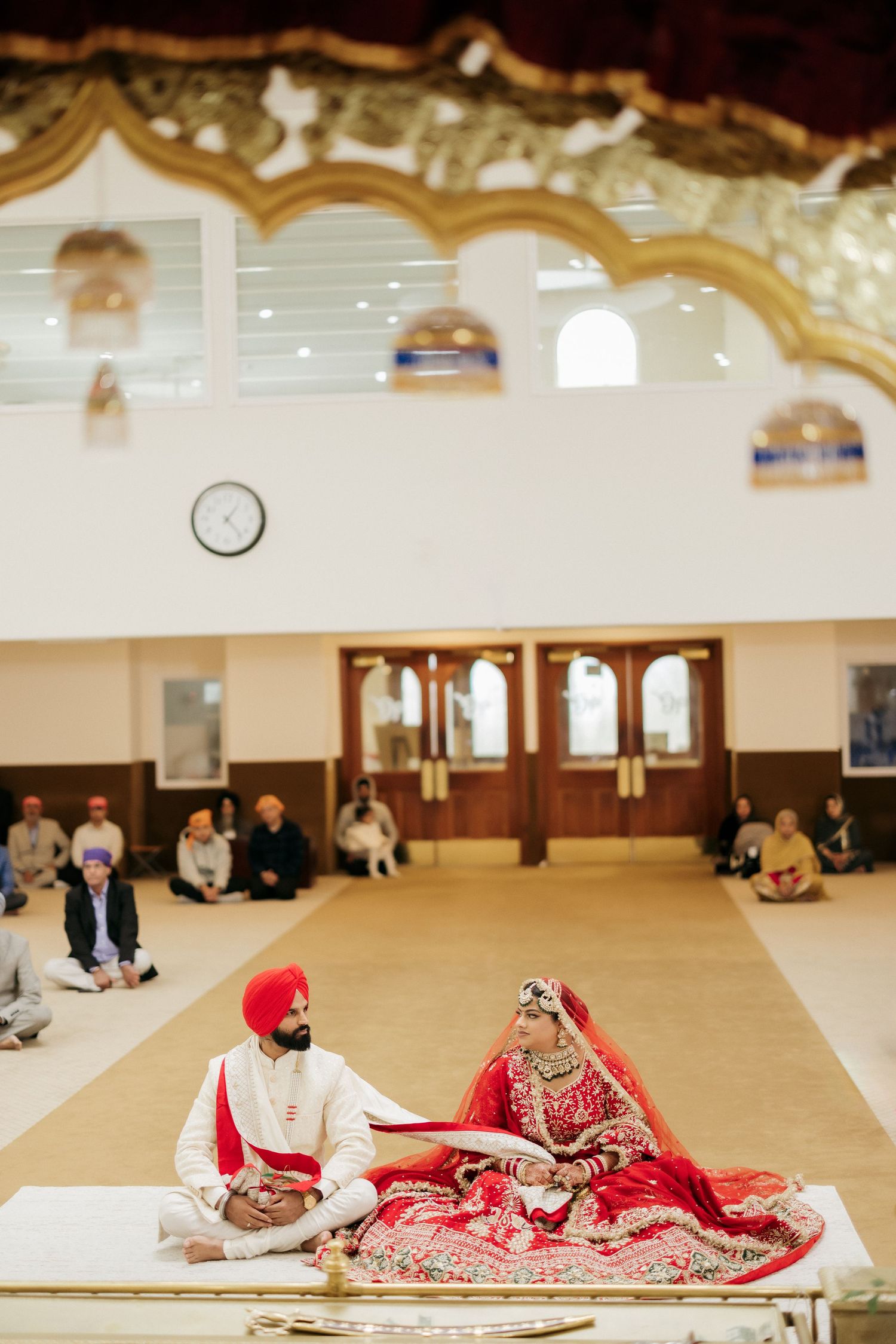 A Sikh wedding ceremony in a temple with decorative arched ceilings and traditional seating arrangements.