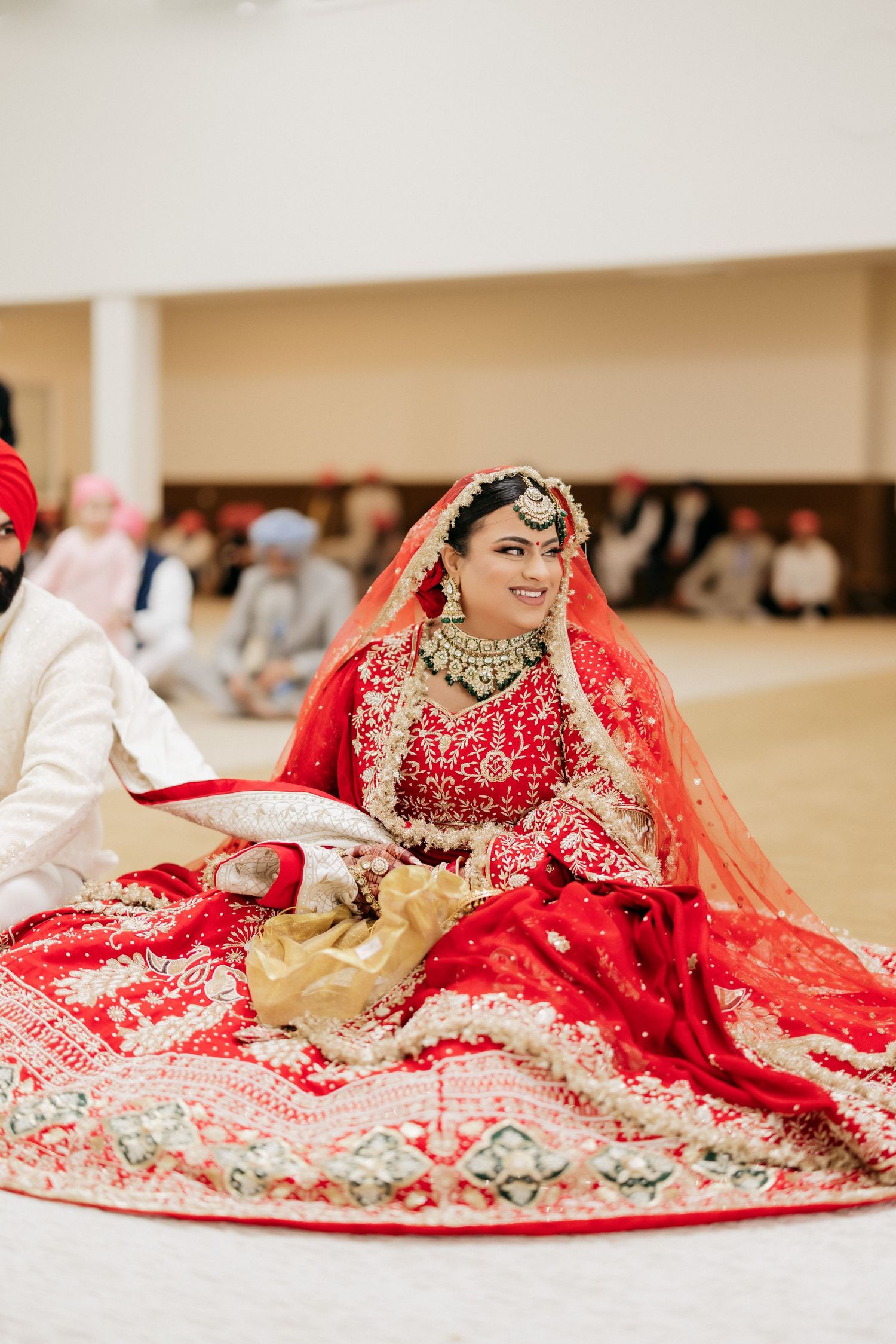 A bride in an ornate red lehenga with detailed embroidery and jewelry during a Sikh wedding ceremony.