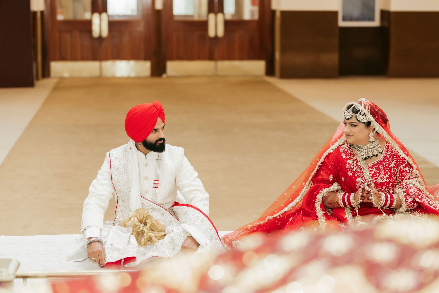 A couple seated during Sikh wedding ceremony with decorative elements in foreground.