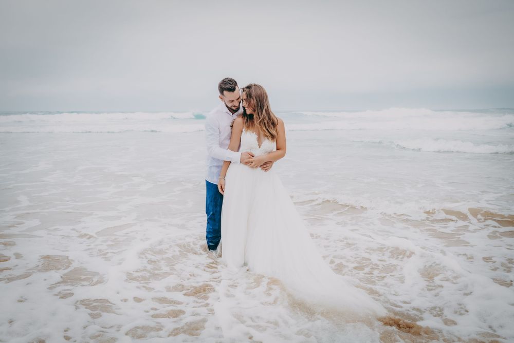Reportaje de postboda en Asturias en la playa, pareja caminando por la orilla con el mar cubriéndoles los pies.