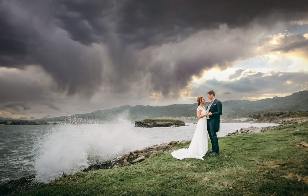 Reportaje de postboda en Asturias junto al mar, pareja abrazada frente a un temporal con olas rompiendo en la orilla de la Playa de la Isla.