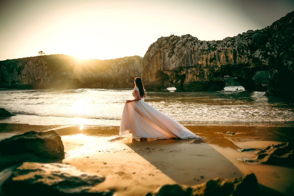 Postboda en Asturias al atardecer, novia caminando por la playa de Cuevas en Ribadesella con el vestido arrastrando sobre la arena.