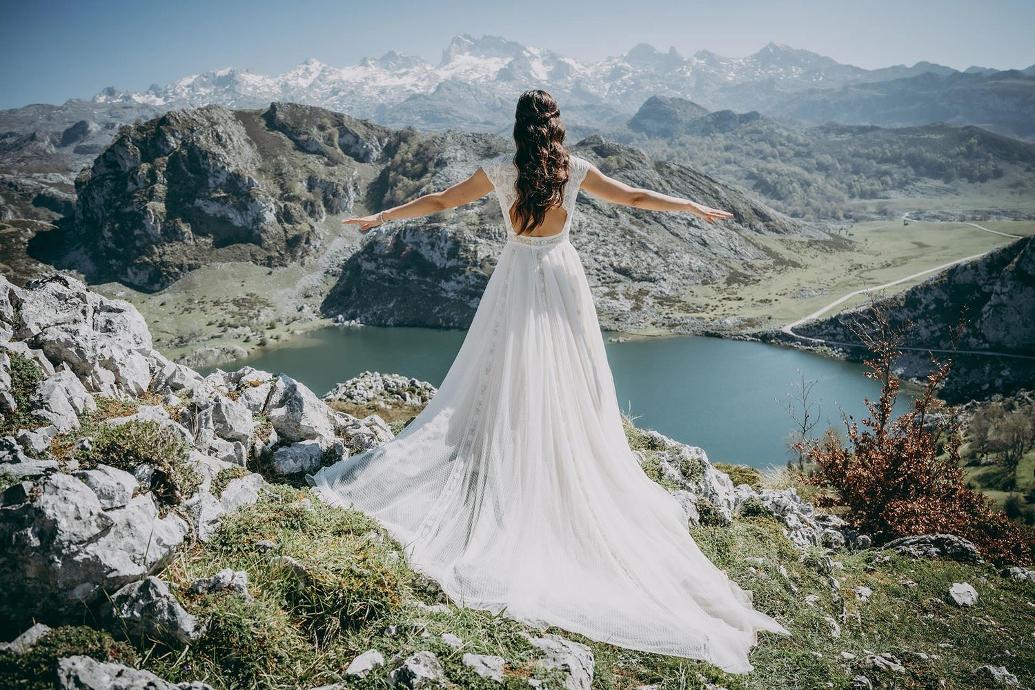 Novia con brazos en alto mira desde lo alto de una montaña a los lagos de Covadonga y a los Picos de Europa en un reportaje de postboda.