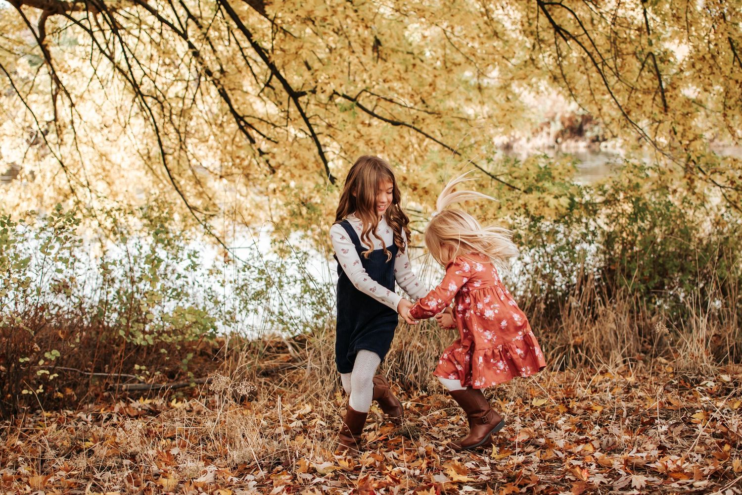 Two children playing together in fallen leaves under golden trees in Tri Cities, Washington.