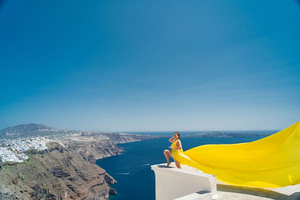 Yellow fabric flows in the wind on a white balcony overlooking the Mediterranean Sea in Santorini.