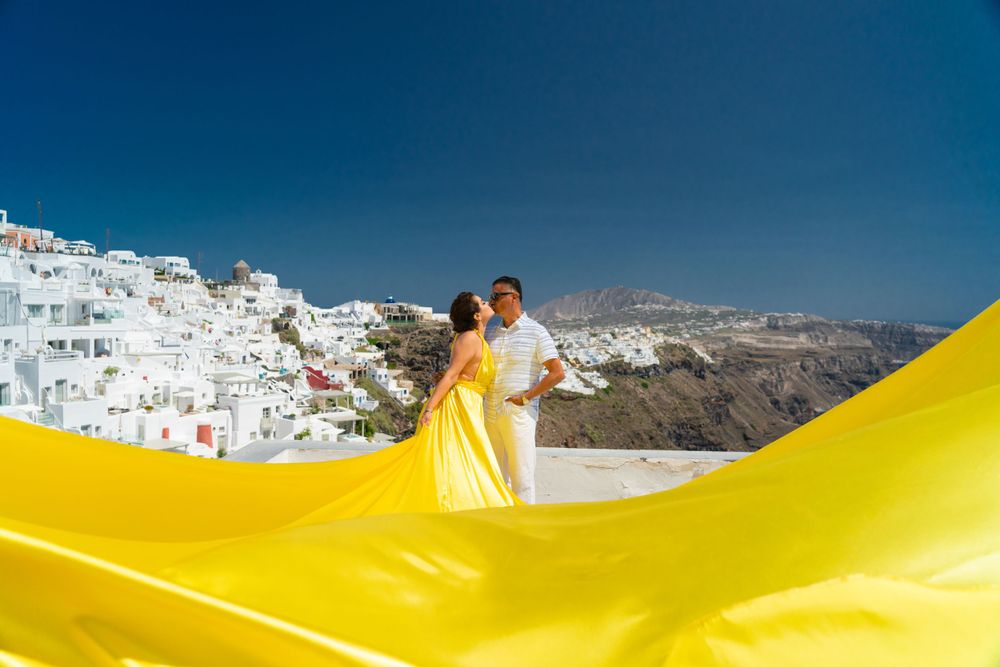 A dramatic yellow fabric flows in front of Santorini's white buildings and blue waters.