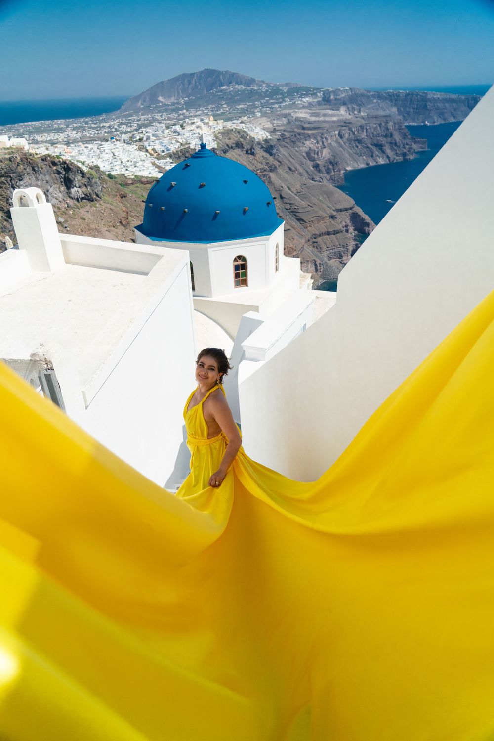 Bright yellow dress fabric flows near iconic blue-domed church in Santorini, Greece.