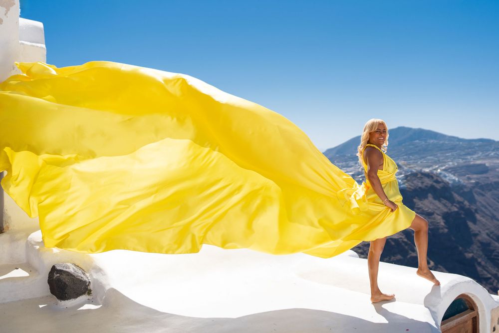 Yellow flowing fabric creates artistic movement against white architecture and blue skies in Santorini.