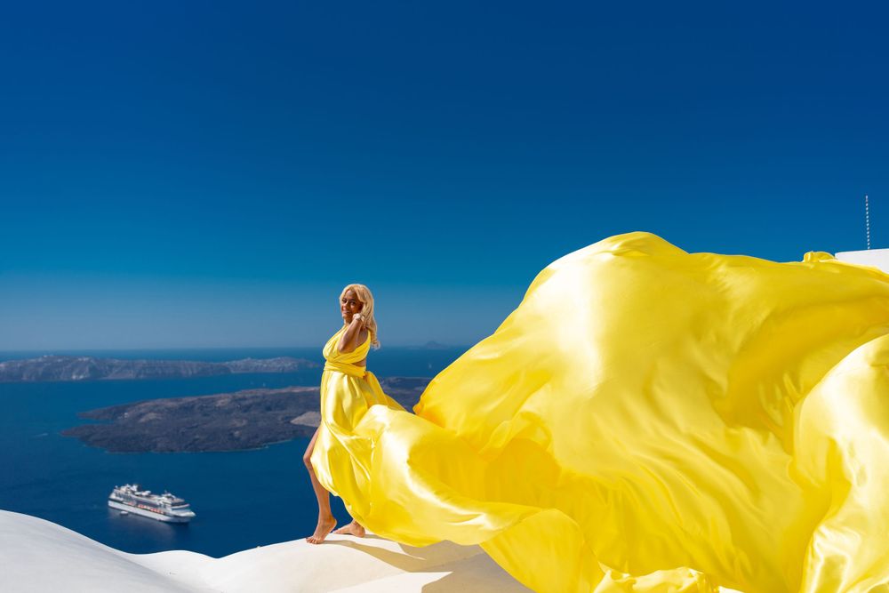 Flowing yellow fabric creates contrast against classic Santorini white architecture and deep blue sea.