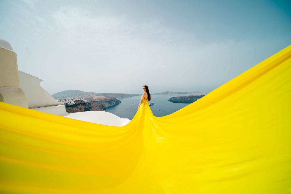 Dramatic yellow fabric flows in the wind against the white architecture and ocean views of Santorini.
