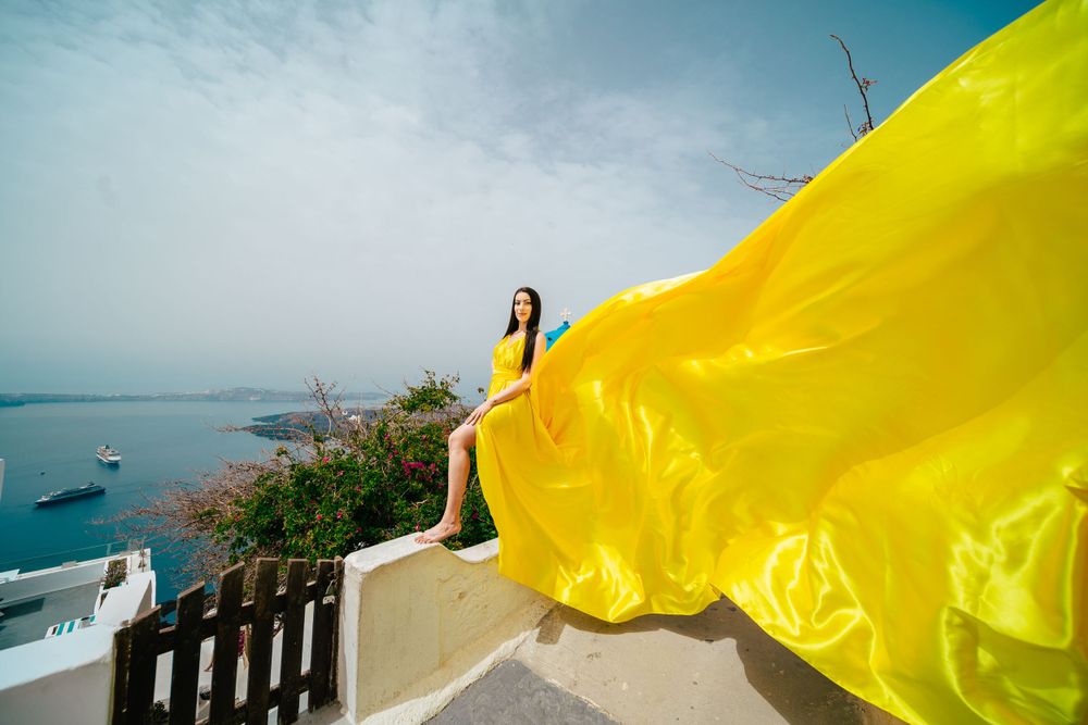 Bright yellow flowing fabric creates dramatic movement against the coastal Santorini landscape.