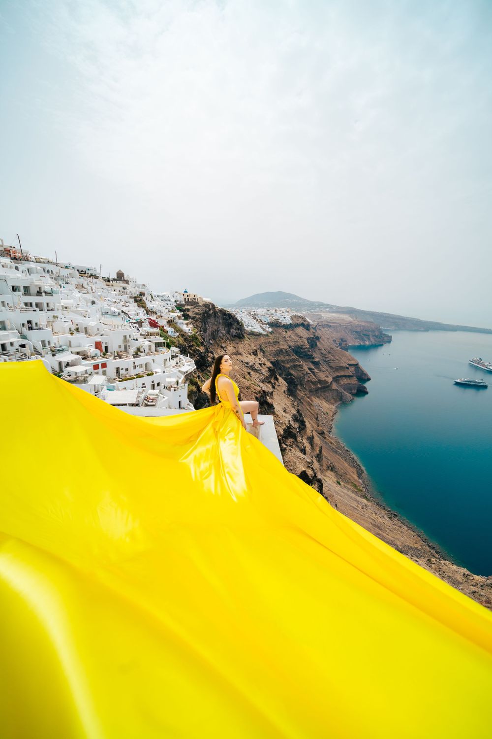 A sweeping yellow fabric contrasts against the white buildings and blue waters of Santorini's coastline.