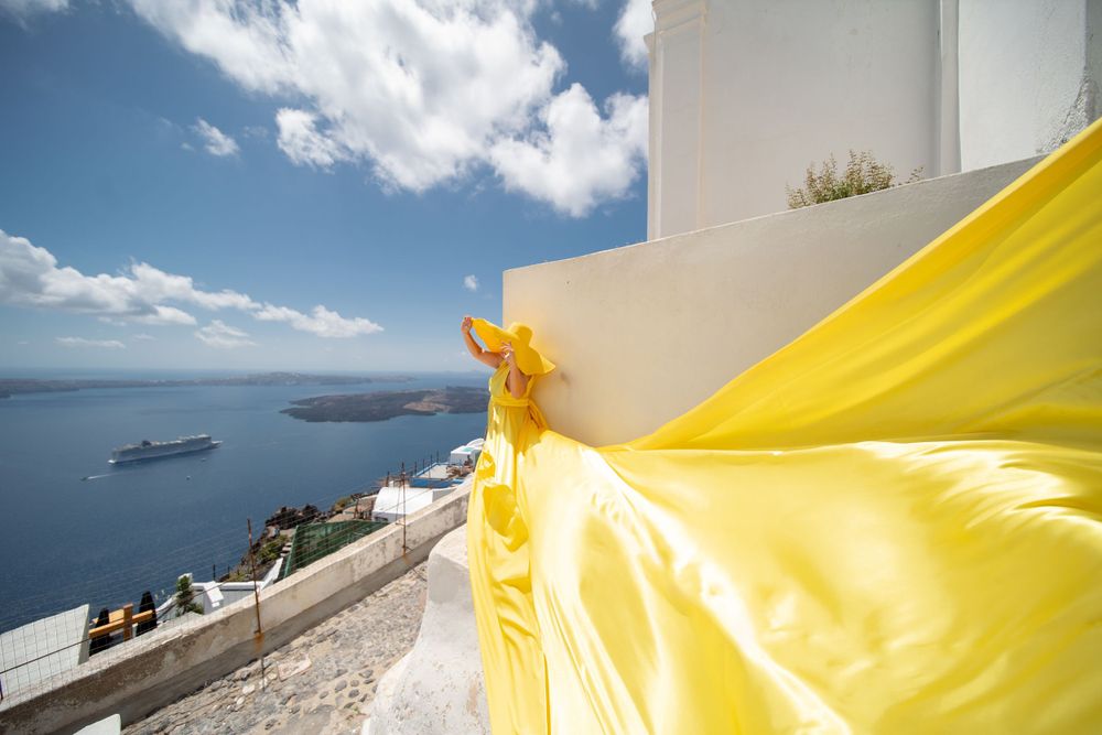 Bright yellow fabric streams in wind against whitewashed buildings and ocean views in Santorini.