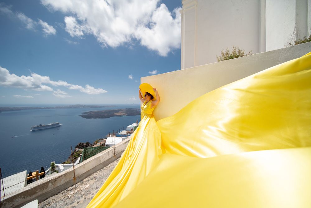 Yellow dress fabric catches wind against classic Santorini landscape with sea view.