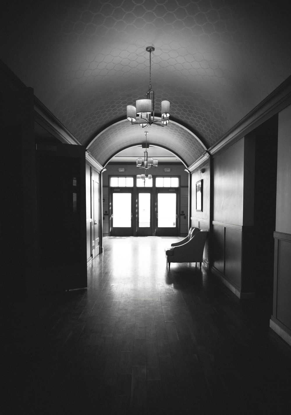Elegant arched hallway with vintage chandelier and dark doors at the end.