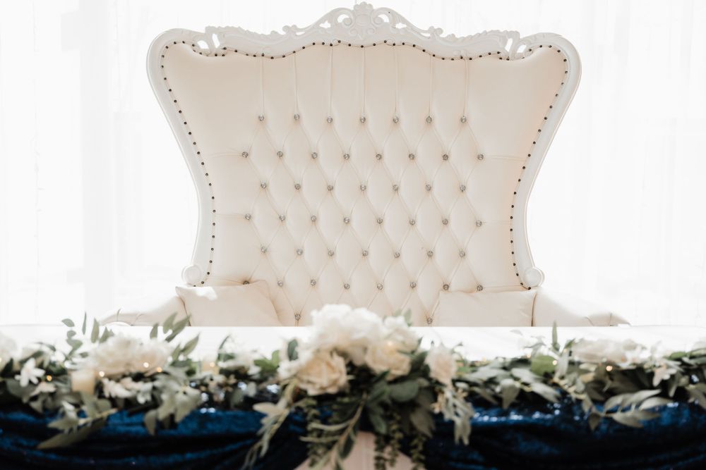 Ornate white tufted loveseat decorated with navy and white floral arrangements.