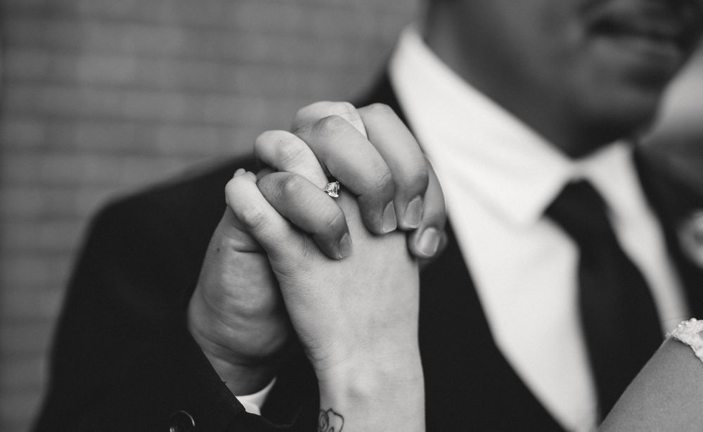 Close-up black and white image of clasped hands with a suit sleeve visible.