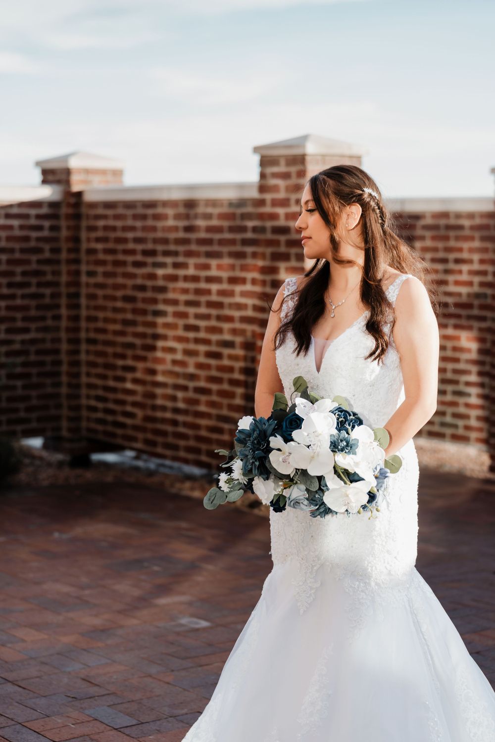 A detailed shot of a bridal gown and bouquet featuring navy and white flowers against brick background.
