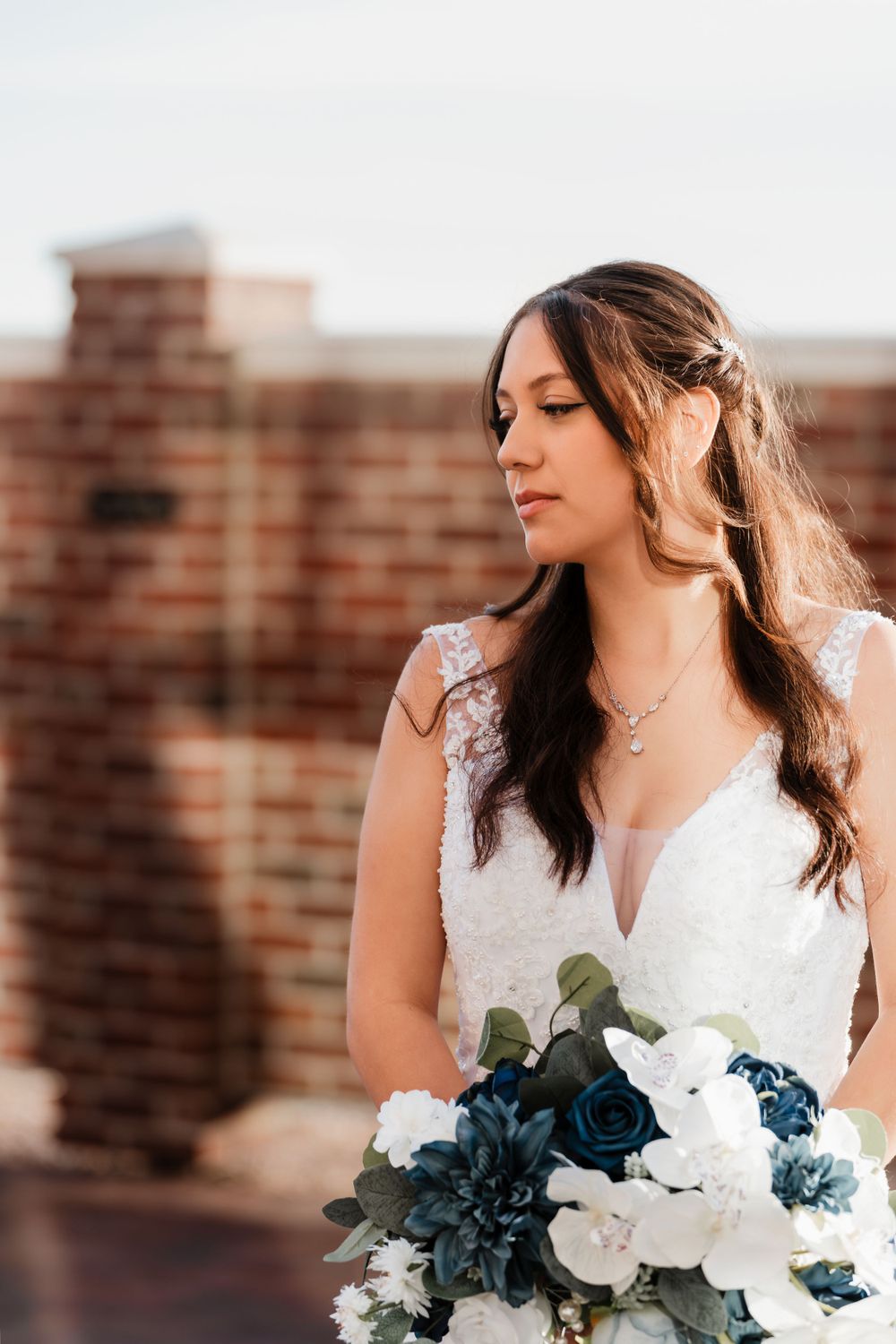 Portrait of a bride in a lace wedding dress holding a blue and white bouquet.