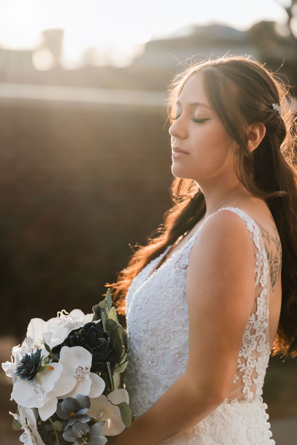 Sunset bridal portrait with white and navy bouquet against warm backlight.