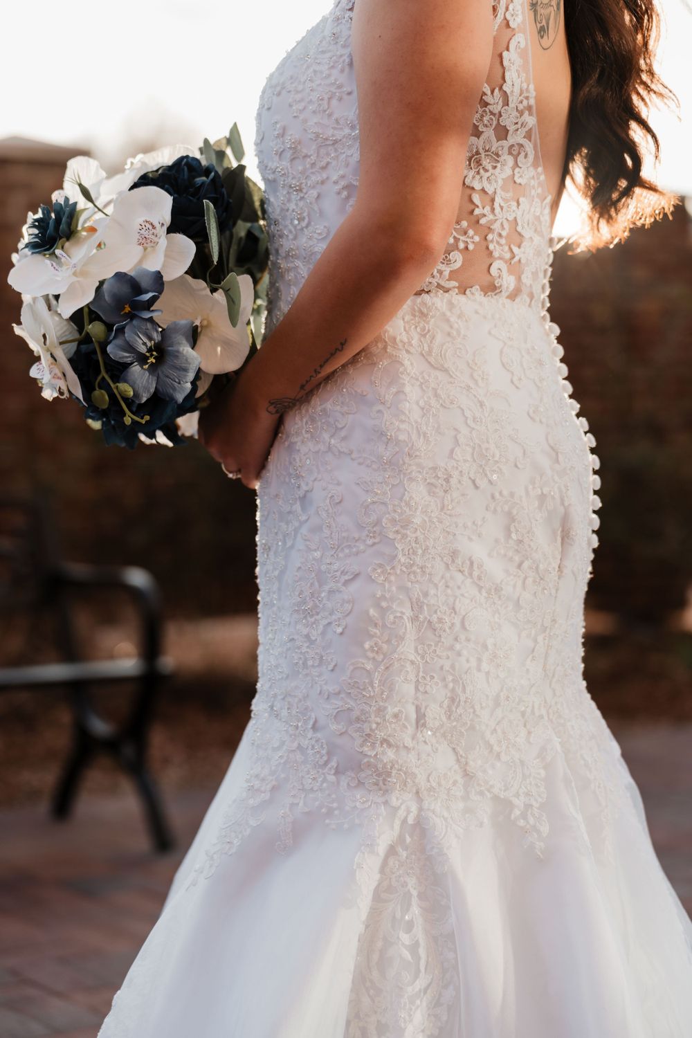 Detail shot of intricate lace wedding dress and white and navy floral bouquet.