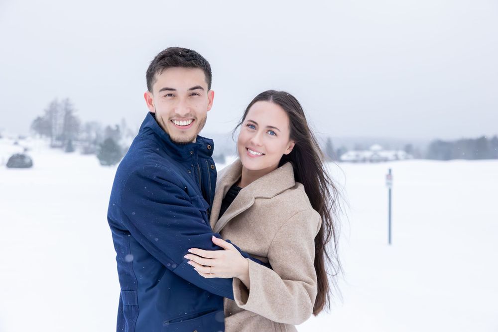 Couple celebrating their engagement in a snow-covered field during winter.