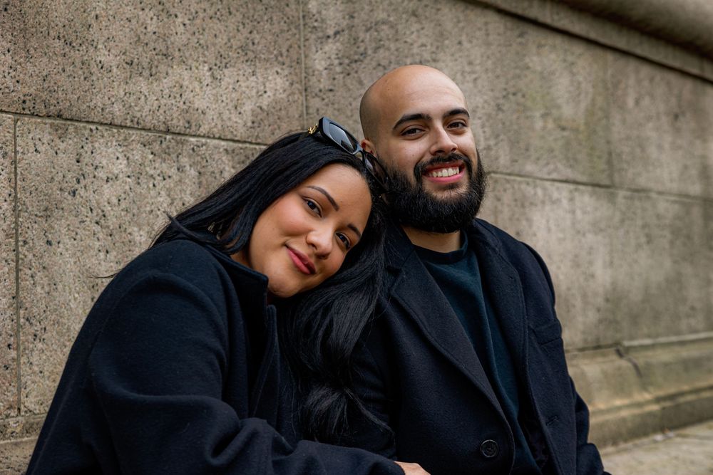 Candid engagement photos showing joyful reactions against concrete wall backdrop.
