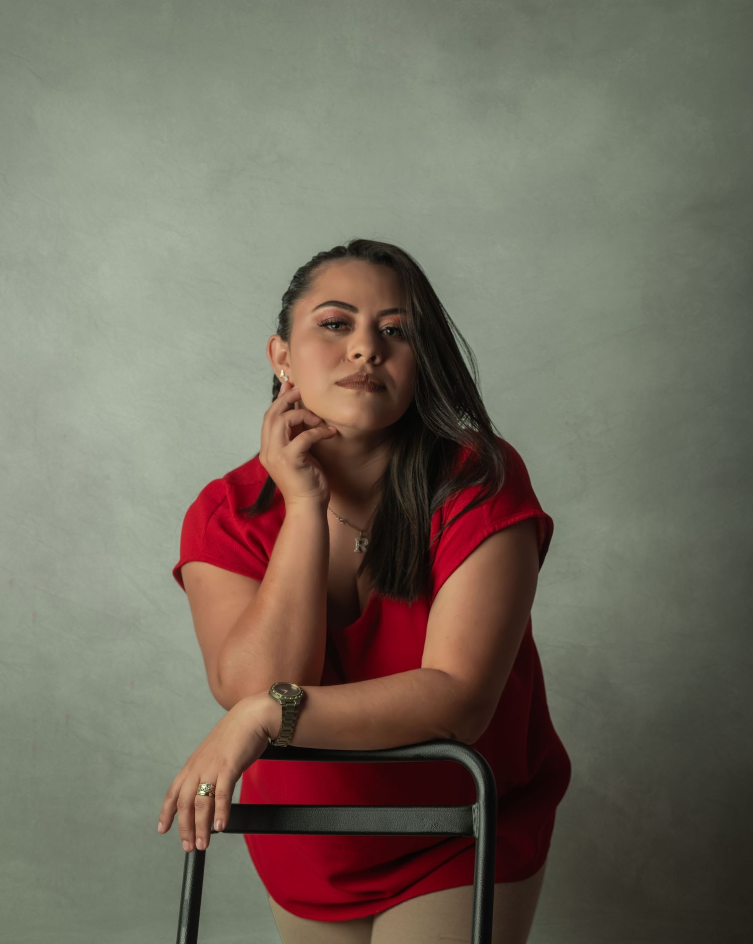 Artistic portrait of a person in a red outfit posed thoughtfully with a chair.