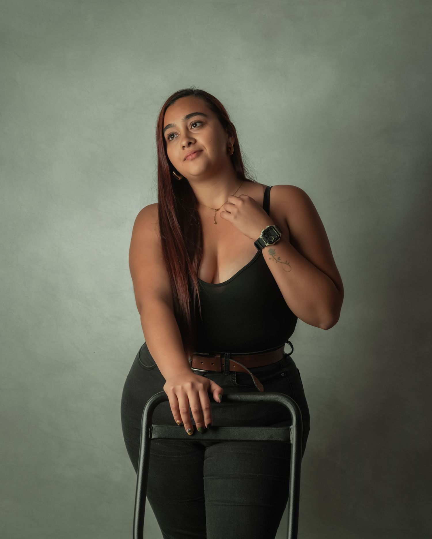 Modern portrait of a woman in black outfit sitting on a chair in a studio setting.